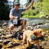 Man with a dog fishing by a river holding a package of treats.