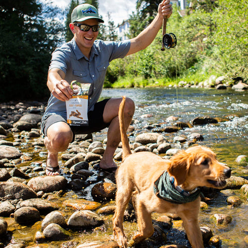 Man with a dog fishing by a river holding a package of treats.