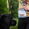 Person holding a package of Smart Cookie dog food with a black dog and fish in the background.